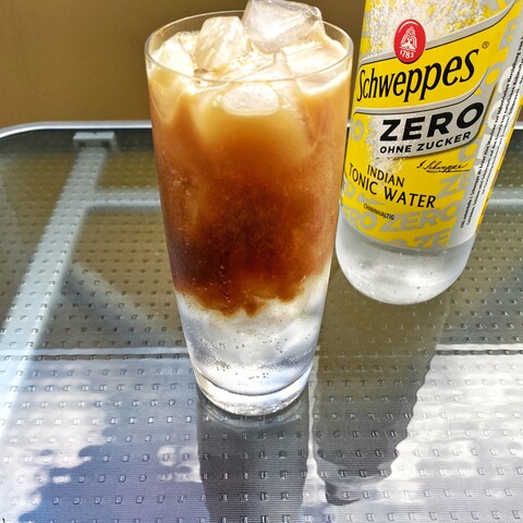 Espresso spreading in a highball glass full of ice cubes and tonic water.