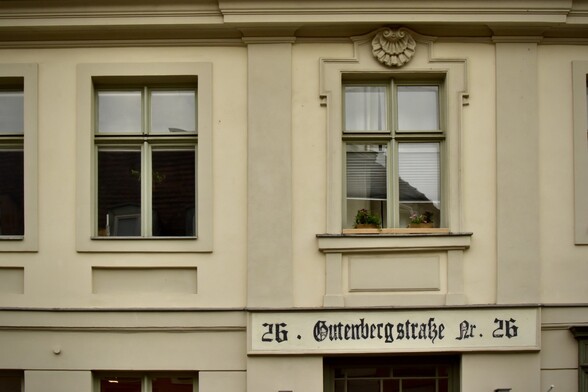 Windows in storefront of faux stone of plaster, sign in Fraktur lettering with street address 