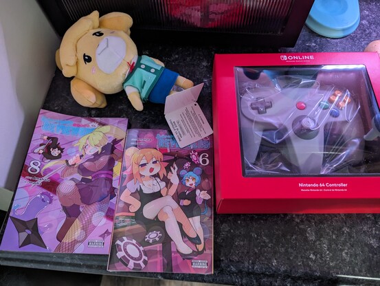 Plush Isabelle, n64 switch controller, and 2 volumes of interspecies reviewers manga