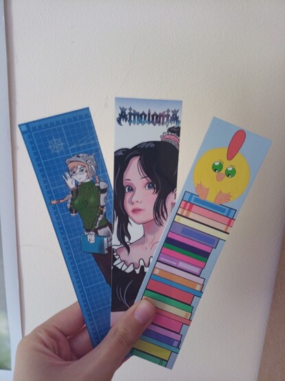 3 bookmarks, girl with blue eyes wearing glasses, metal helmet and holding book, girl with black hair and blue eyes looking at us, round yellow chicken with green eyes sitting on books