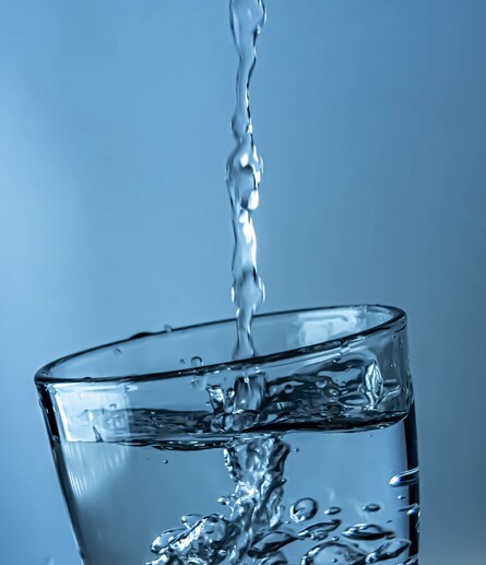 Clean water streaming into a clear glass with a blue background.
