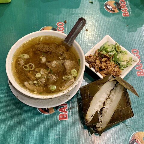 A bowl of coto Makassar with ketupat (rice cake) and onion condiments 