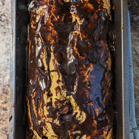 Image shows a loaf of peanut butter bread topped with chocolate in a silver bread pan.