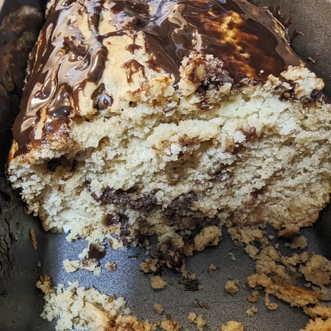 Image shows a loaf of peanut butter bread with chocolate chips in it and chocolate on top with a slice taken out in a silver loaf pan.