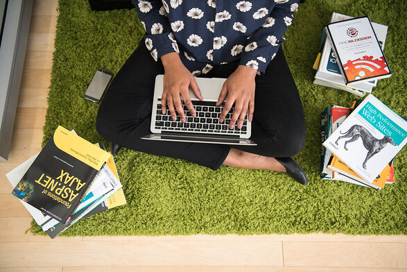 A photograph of a woman’s cross-legged lap, with a MacBook resting on it. She is surrounded by books like “High Performance Web Sites” and “ASP.Net Ajax.” Her skin color is relatively dark (true of most of the photos in the collection).