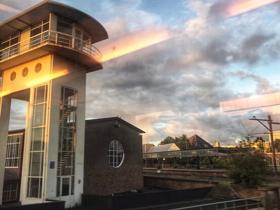 view from a train, the reflection of lights inside the train on the window, outside is a white, tower-like building, the style clearly from about a century ago 