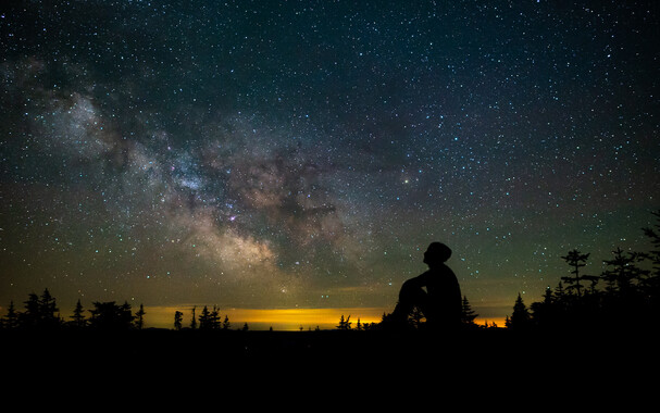 Silhouette of a man sitting against a sky filled with stars and the Milky Way. 