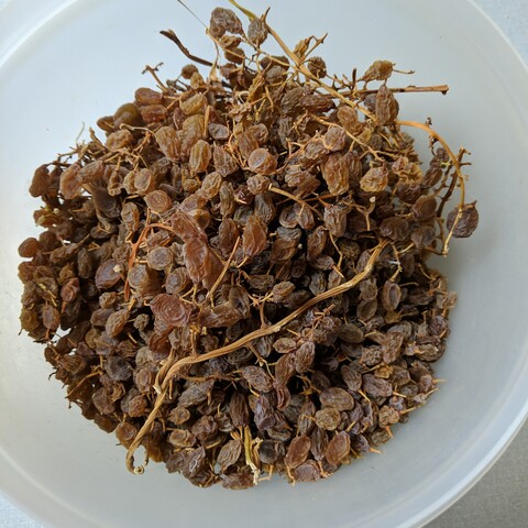 Dehydrated green seedless grapes that are darker but not as dark as a sun dried raisin. They still have stems attached. They are in a white bowl.