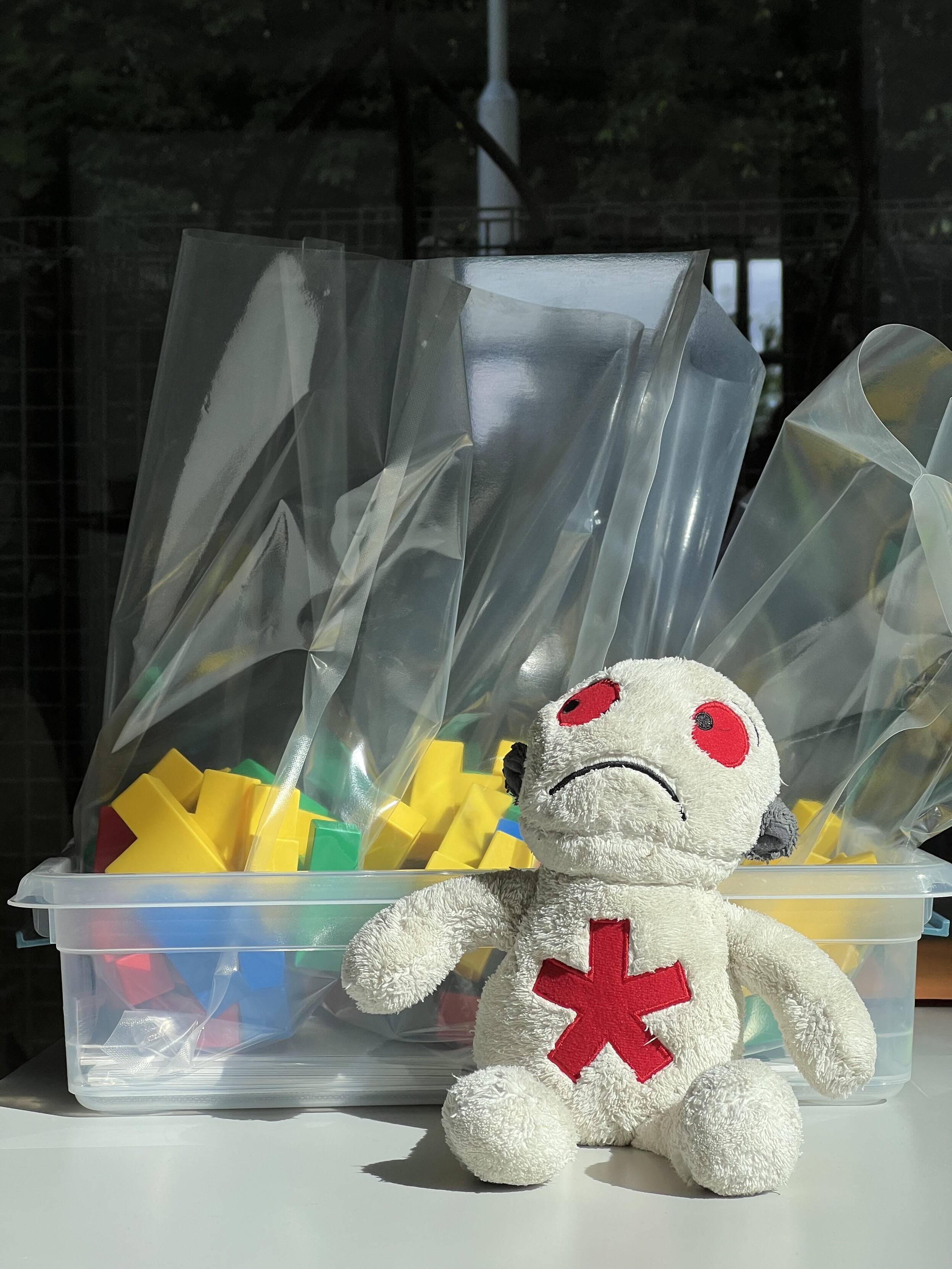 A sad stuffed animal in sunlight, sitting in front of bags with colorful blocks