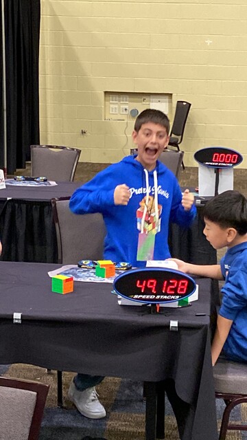 An elated little duder having just finished solving a 4x4x4 rubiks cube, showing a score on the timer of 49.128s