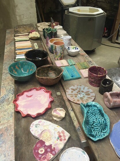 Fertige bunt glasierte Töpferwaren stehen auf einem Tisch in der Werkstatt.