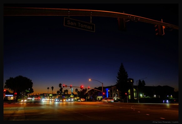 a street crossing at dusk in, with cars waiting on the red light and palm trees and a motel neon sign in the background