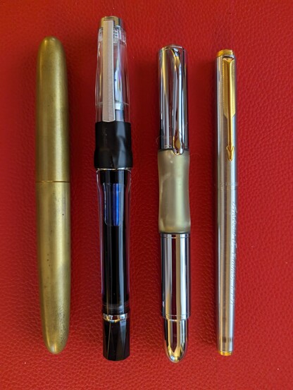 Four posted fountain pens arranged side-by-side on a textured red mat.
