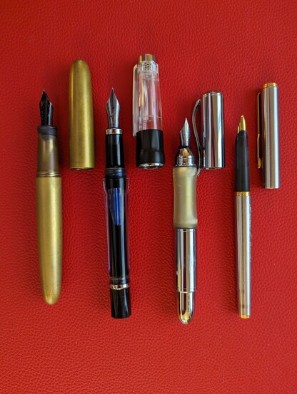 Four fountain pens with caps removed arranged side-by-side on a textured red mat.