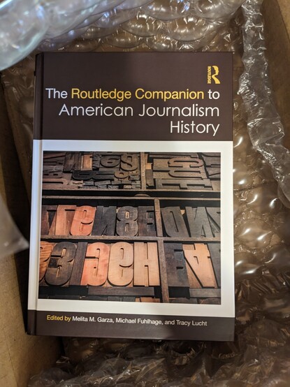 A copy of The Routledge Companion to American Journalism History, edited by Melita M. Garza, Michael Fuhlhage, and Tracy Lucht, sitting inside its shipping container during the unboxing of my author's copies.