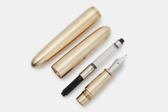 A product photograph of a disassembled Ensso PIUMA brass fountain showing the barrel, cap, cartridge converter and the grip section and nib.
