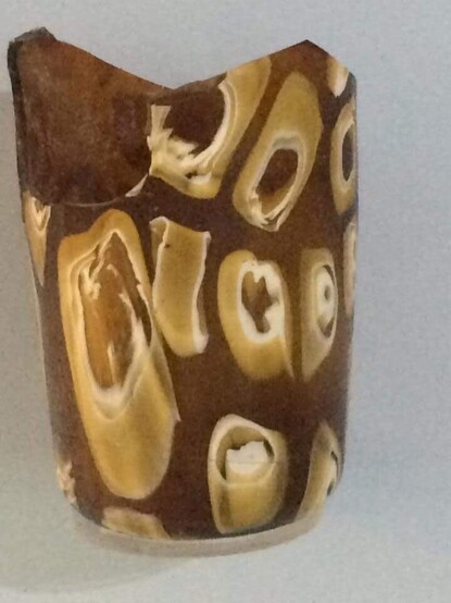 Narrow cylindrical glass vessel in dark amber glass with with and yellow tubular millefiori 'eyes'.
