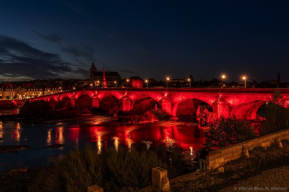 Pont Jacques-Gabriel illuminé en rouge, avec l’Hôtel de Ville également illuminé en rouge derrière lui, photographiés en aval.