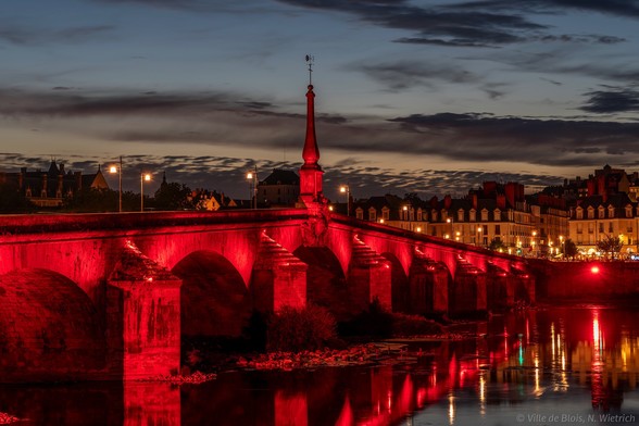 Le pont Jacques-Gabriel illuminé en rouge photographié de près. La flèche rouge coupe le ciel.