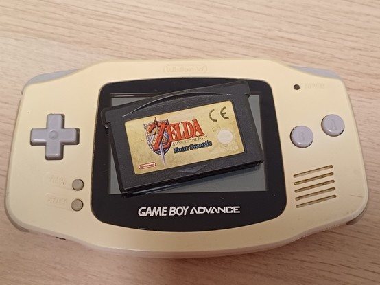 A "Nintendo GameBoy Advance" in white(yellowed) with a game cartridge of "The Legend of Zelda - A Link to the Past" centered on the screen.