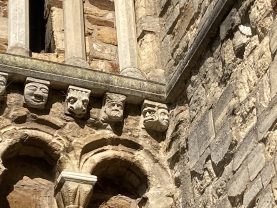 12th century exterior carvings on St Peter’s church Northampton a row of carved heads some looking like animals along a course of rich northampton ironstone on the outside of the bell tower. 