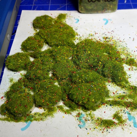 13 lush piles of static grass with pieces of coloured plastic in up make it look like a flowery meadow. Somewhere below that are 25, 32 and 40mm bases