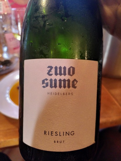 Sektflasche mit etwas Feuchtigkeit auf dem grünen Glas. Etikett: "Zwo Sume, Heidelberg, Riesling, Brut"

Dahinter ein Teller mit Kürbissuppe.
