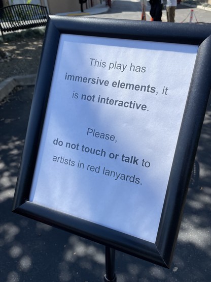 Sign reading:

“This play has immersive elements, it is not interactive.

Please, do not touch or talk to artists in red lanyards.”