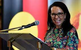 Happy Minister Burney stands before the Aboriginal Australian flag and her microphone 