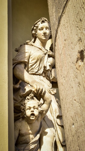 Female neoclassical statue with cherub, peeking out from behind two stone columns