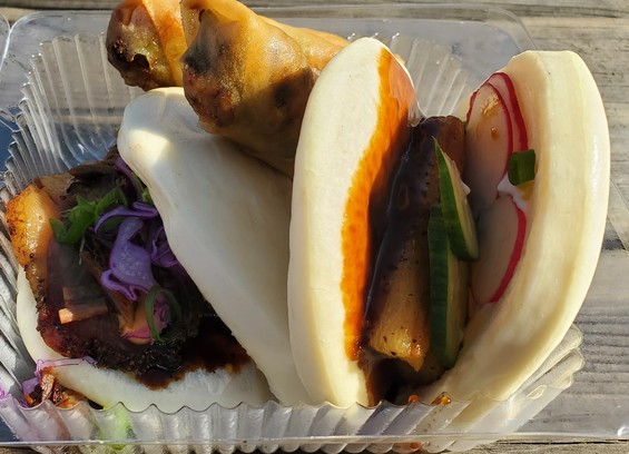 A tray with two bao buns filled with meat and veggies, between the two is a fried spring roll.