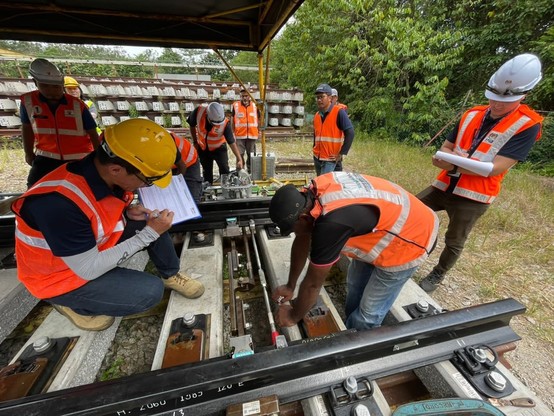 Two people measuring something on the railway track while the other people are observing something else.