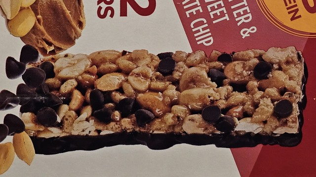 Picture of a protein bar on the side of a package, with many chocolate chips visible all across the bar.