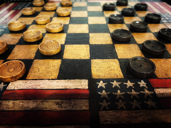 A vintage handmade wooden checkerboard and checkers decorated with a border of American flags for a touch of americana.