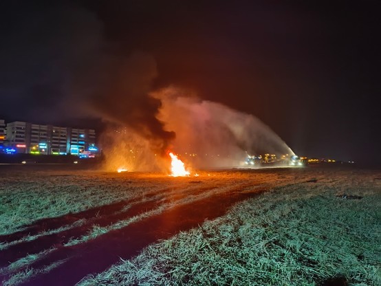 A fire on a field, with fire truck spraying water from a distance.