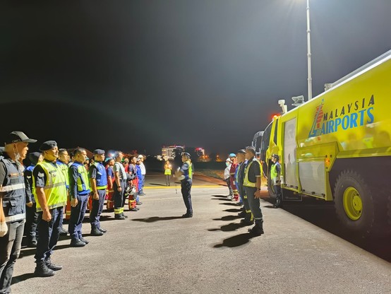 A group of people standing in rows of lines in front of airport emergency vehicle.