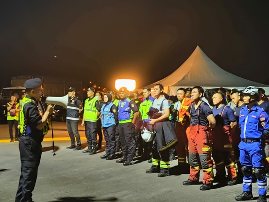 A person handling a loud speaker and a group of people listening to the command.