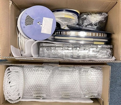 Two boxes. Box on top has reels of components. Box at the bottom contains reels of assembled Bus Pirate 5 baords wrapped in bubble wrap.
