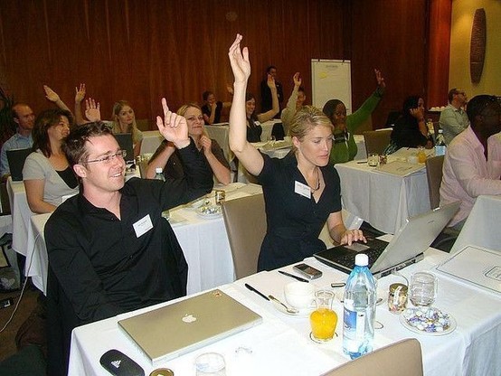 right way to vote: photograph of conference attendees sitting in front of tables, raising their hands to vote