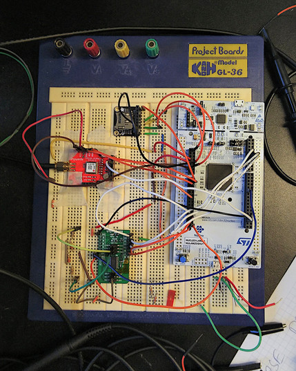 An electronic prototyping breadboard mit a STM32 Nucleo-L496ZG board, a micro-SD-, GNSS module and an ADC breakout board. Many jump wires connect the breakout boards with the Nucleao board.