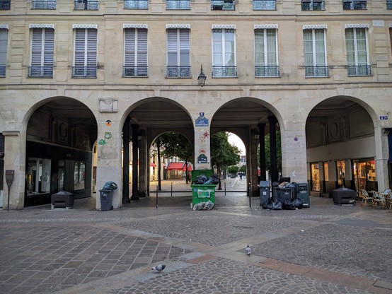 Four arches form an arcade in central Paris. Trash overflows from bins against the dividing columns, while street art climbs the walls.