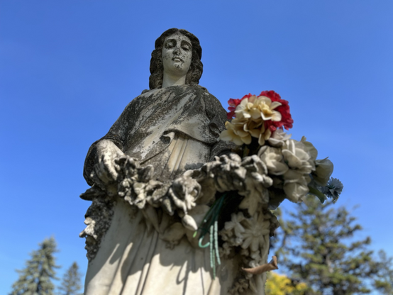 Stone cemetery angel holding red and white plastic flowers against a clear blue sky. 