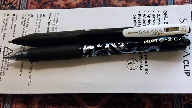 Two gel ink pens, A Zebra Sarasa Clip 0.7 and a Pilot G2 0.7. The Sarasa has a black barrel with an ivory colour clip, and the Pilot has an ornate silver and black pattern called Victoria.