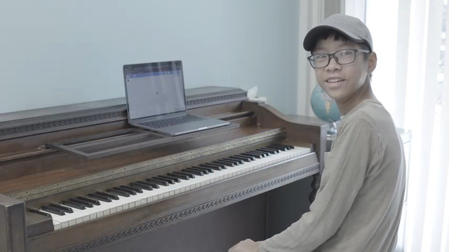 Student smiling at piano with computer displaying a metronome application.