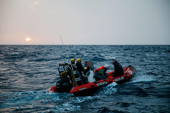 Das RHIB auf dem Meer, die Sonne geht gerade unter, auf der Seite steht groß auf dem orangen Schlauch IUVENTA RESCUE. Vier Leute sind an Bord.