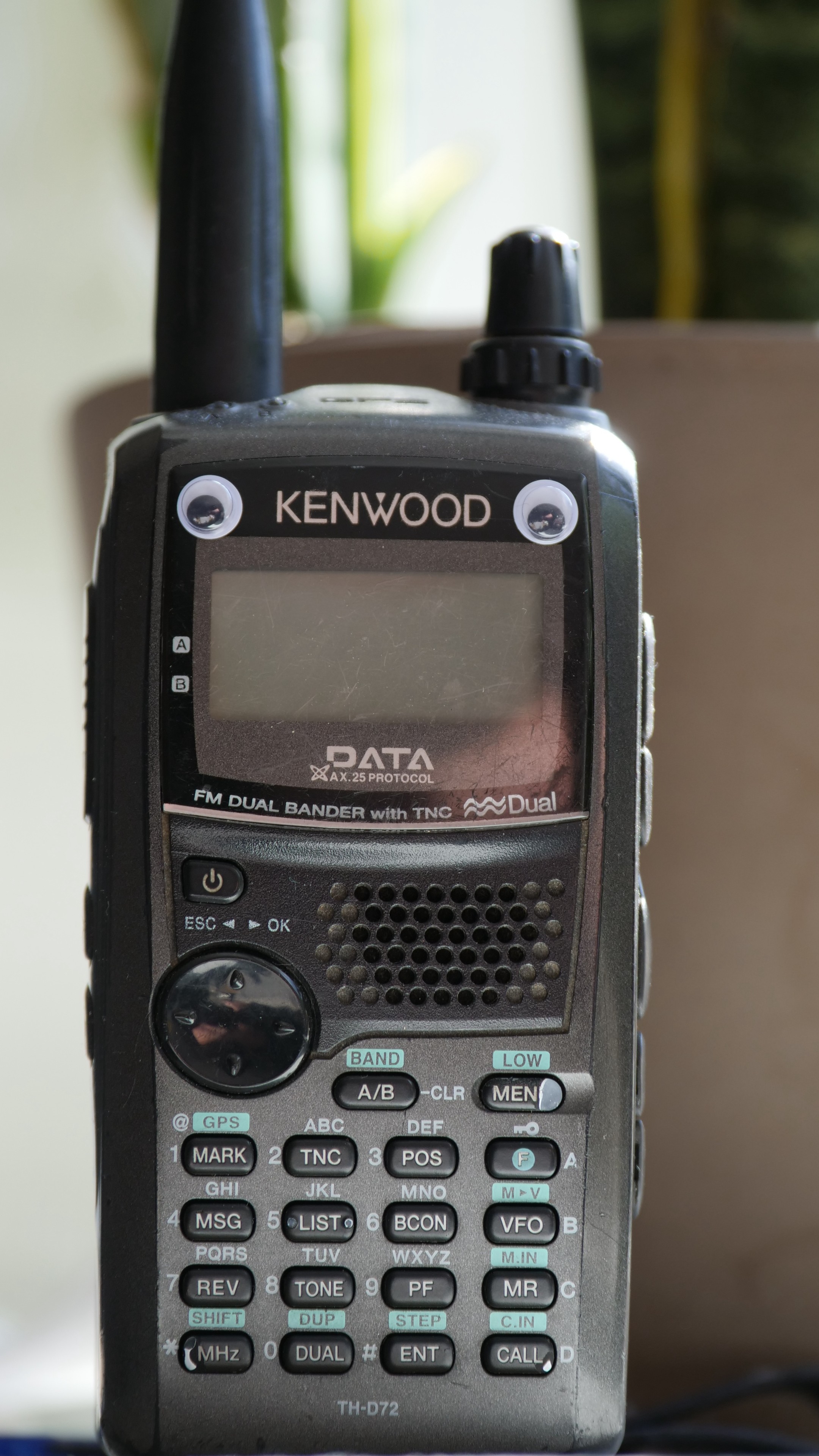 Kenwood TH-D72 hand held transceiver, pictured from the front, but now with googly eyes added on the top