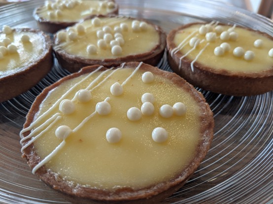 A glass plate of lemon tarts, garnished with white chocolate pearls.