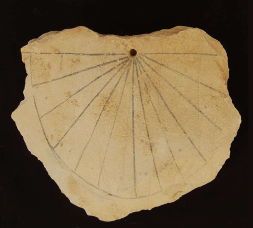 Flat piece of limestone with the twelve hour lines of a sundial painted on the front.