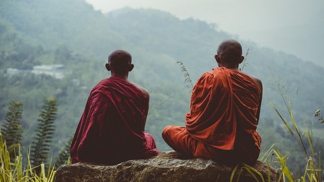Two Buddhist monastics meditating on a rock.