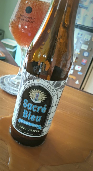 Sacre Bleu Barrel Aged Tripel by Craftwork Brewery in Oamaru, New Zealand. Puddle of craft beer around the bottle as the beer was so excited to leave the bottle (gusher).